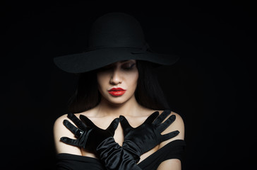Fototapeta na wymiar Woman in big black hat with arms across, studio portrait, dark background