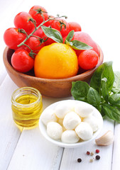 yellow and red tomatoes, garlic, basil and mozzarella cheese on a white wooden background