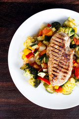 Grilled chicken fillet, breast with cooked vegetable Tomatoes, Carrots, Peppers, Courgettes, brocoli on plates.