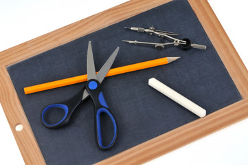 Compas, crayons à papier, ciseaux et craie posés sur une ardoise