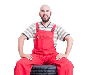 Happy smiling mechanic sitting on stack of car wheels