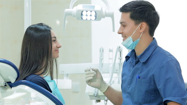 Dentist holding a tool and explains the girl patient