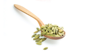 Lots of cardamom pods on wooden spoon isolated on white backgrou © gulchuk_ua