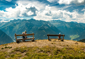 family relaxing on benches in autumn austrian mountains with peaks view