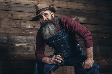 Vintage worker man with long gray beard in jeans dungarees holdi