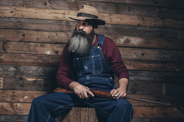 Vintage farmer holding rifle sitting on wooden crate in barn.