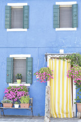 Blue painted wall with several windows with green wooden shutters, at the island of Burano, Venice, Italy