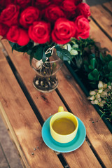 Cup of green tea and a bouquet of roses on a wooden table
