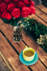 Cup of green tea and a bouquet of roses on a wooden table