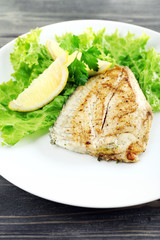 Dish of fish fillet with lettuce and lemon on table close up