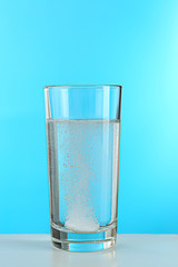 Pill in glass of water on blue background