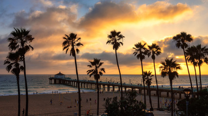 Palmbomen over het strand en de pier van Manhattan bij zonsondergang in Los Angeles.