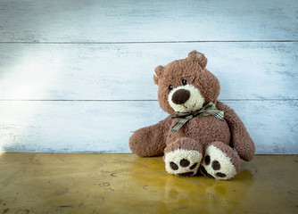 Lonely teddy bear sitting on the floor with space on wood background