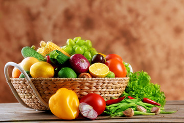 Heap of fresh fruits and vegetables in basket on wooden table close up