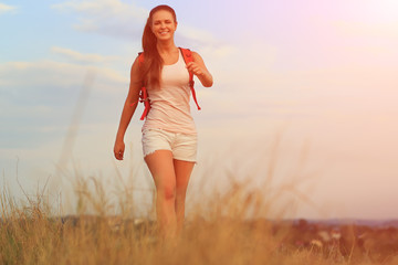 Young woman with red backpack walking on sunset summer.