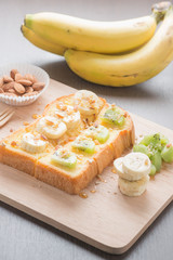 Toast topped with banana ,kiwi, almonds and honey on the wooden
