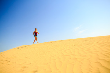Fototapeta na wymiar Young woman running on sand desert dunes