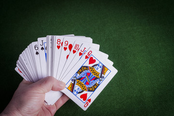 Male hand holding pack of cards on green felt background