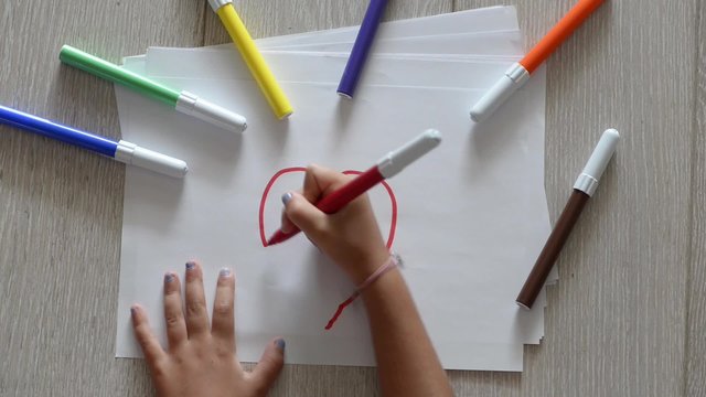 Young girl draws a red heart on a white sheet with a red marker