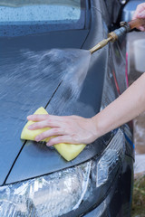 Human hand with sponge soap washing red car surface