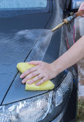 Human hand with sponge soap washing red car surface