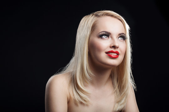 Fashion Stylish Beauty portrait of smiling beautiful blonde girl with professional make-up, false eyelashes and red lips on dark background