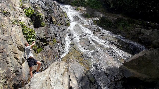 Young Man Taking Photo of Waterfall by Mobile Phone Outdoors