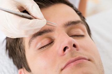 Fototapeta na wymiar Beautician Hands Plucking Man Eyebrows With Tweezers