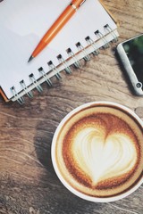 Blank notepad and smart phone with latte art coffee on office table