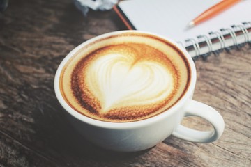 Blank notepad and pen with latte art coffee on office table