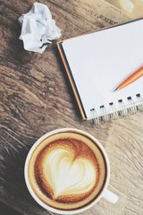 Blank notepad and pen with latte art coffee on office table