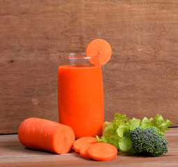 Fresh carrot juice with vegetables on wooden background