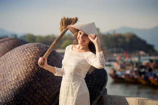 Blonde Girl In Vietnamese Dress Holds Besom On Embankment