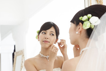 Bride wearing earrings while looking in the mirror
