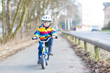 Fototapeta na wymiar kid boy in safety helmet and colorful raincoat riding bike, outd