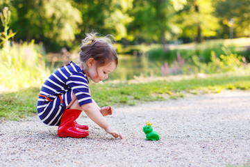 Beautiful little girl in red rain boots playing with rubber frog