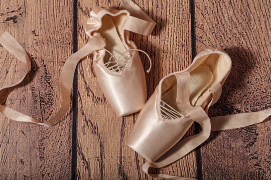 Ballet pointe shoes lie on wooden floor.
