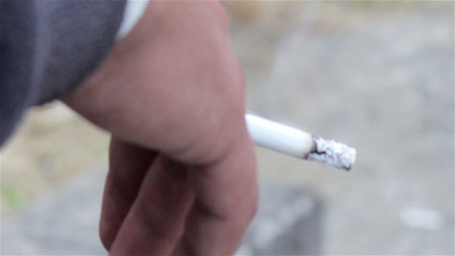 smokes cigarette in hand/man holding a cigarette with smoke which burns