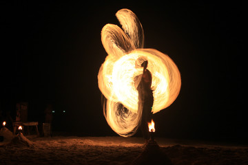Fire-dancing in slow speed shutter photography on the beach - obrazy, fototapety, plakaty