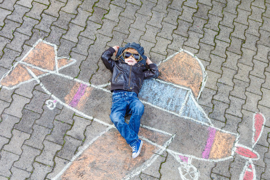 Little boy having fun with airplane picture drawing with chalk