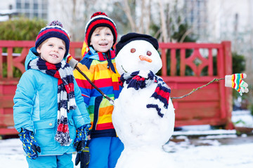 Two little friends making a snowman, playing and having fun with