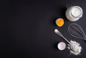 eggs, flour, milk and whisk on a dark background