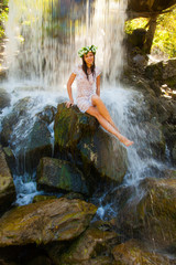Naked girl in a wreath and a white dress at the waterfall.