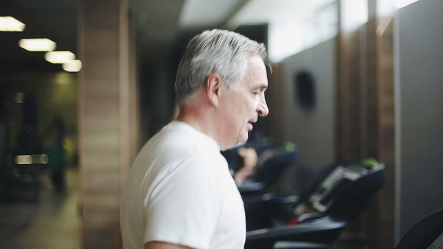 Senior man exercising on a treadmill in the gym. Right profile face footage