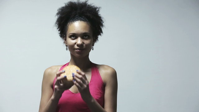 Attractive african american woman eating big burger at gray background in studio