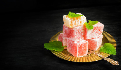 Turkish delight on oriental metal plate on black background. Concept of oriental sweets with space for text           