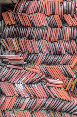 Pile of old black and orange tiles covered with dirt and cobwebs, left after renovation of old church roof