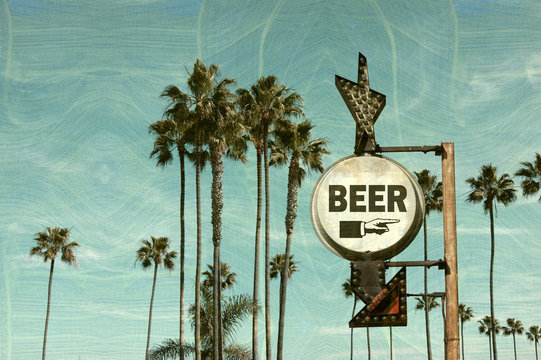 Aged and worn vintage photo of beer sign on beach with palm trees