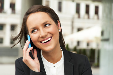 Business woman talking by phone against the glass wall in the ci