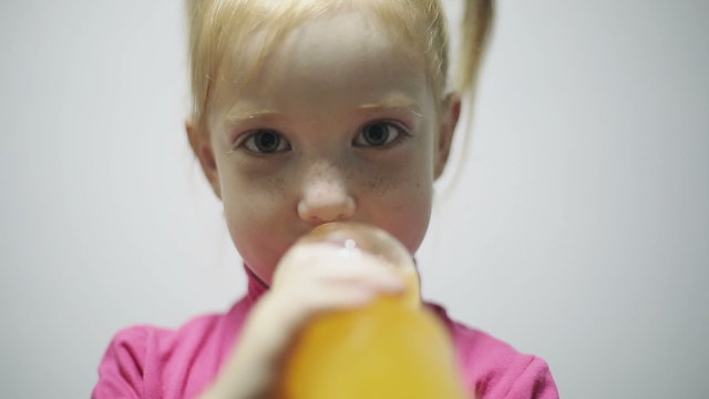Child drinking orange beverage at gray background in a studio